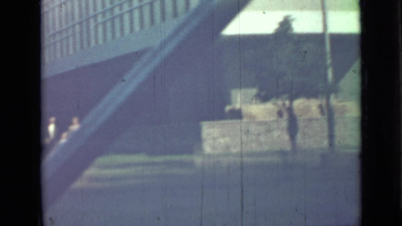 Large building exterior with diagonal stair or ramp, low wall, and small distant figures.