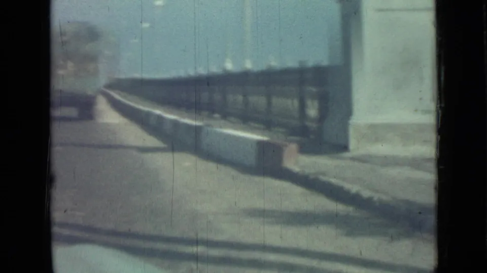 The final frame shows a dark roadside railing, a white pillar, pavement, and soft 8mm grain during the moving drive.