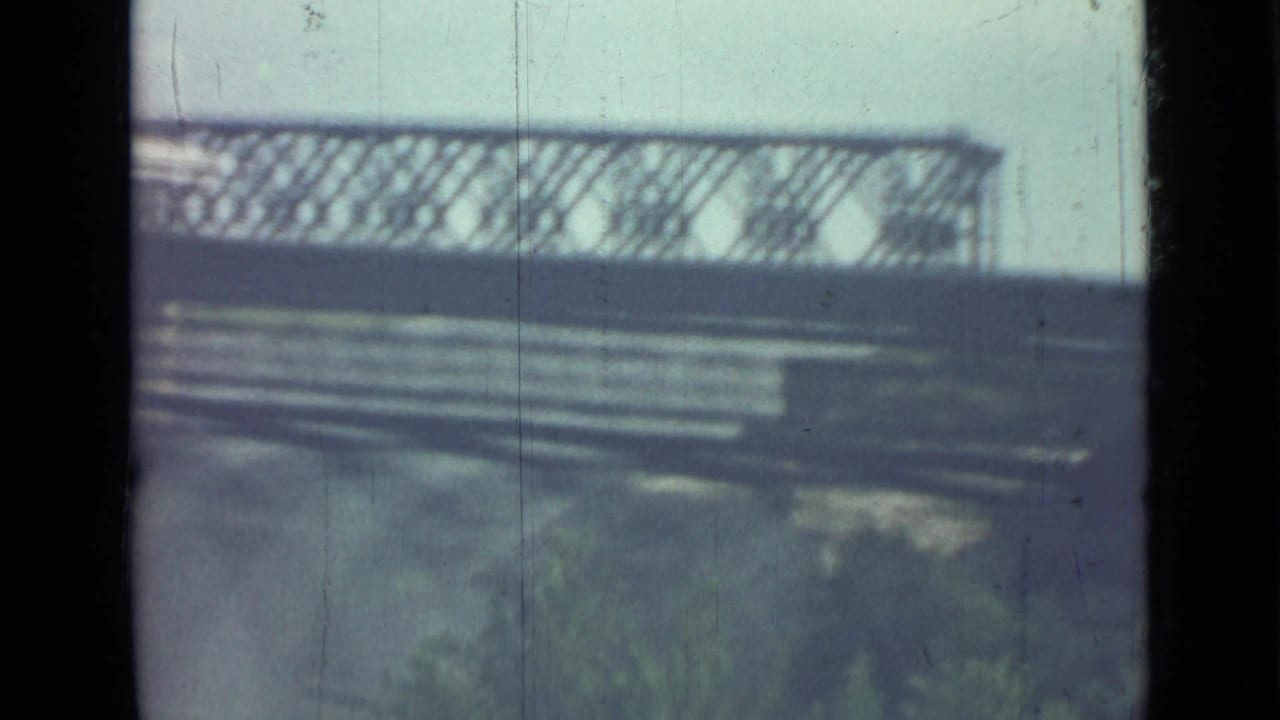 Blurred view through a dark vehicle window with railings and pale outdoor shapes.