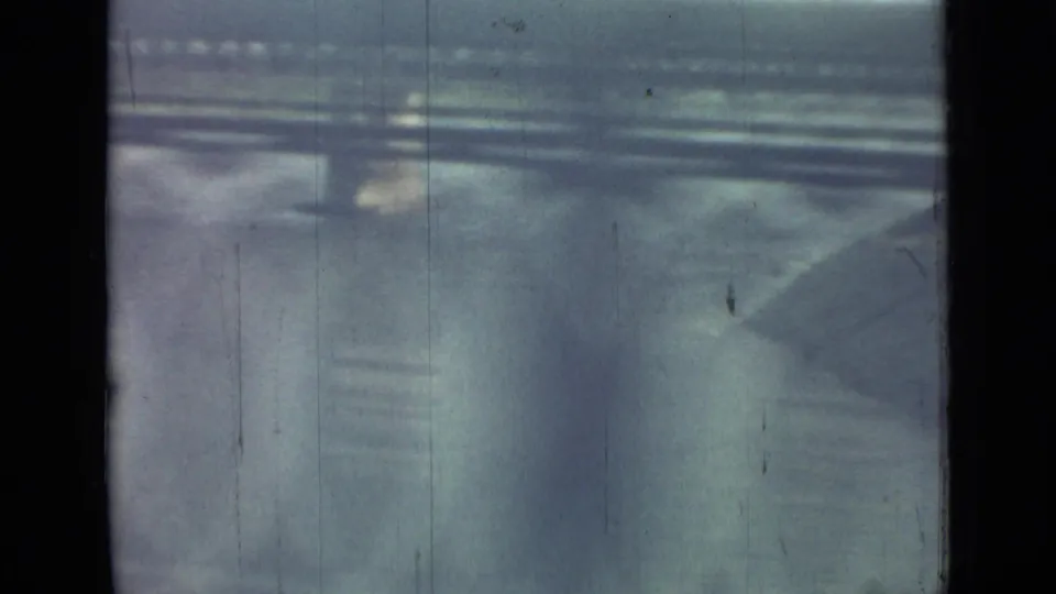 A divided window frames a fast, indistinct exterior view in 1967 Saint Petersburg, with horizontal structures and pavement-like surfaces.