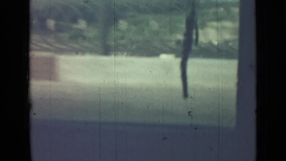 A passing Saint Petersburg exterior view shows greenery, a pale wall or barrier, and a dark vertical pole through faded 8mm film texture.