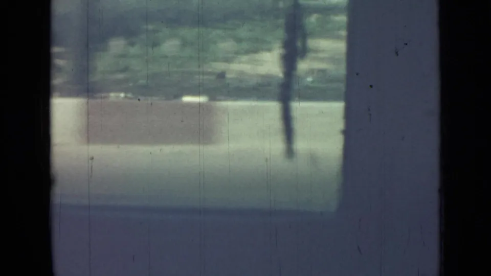1967 Saint Petersburg home-movie frame looking from inside a moving car through dark window pillars toward a sunlit roadside.