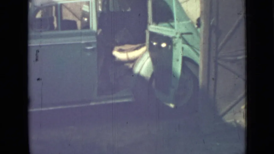 1967 home-movie frame from Saint Petersburg showing a blue van with its rear door open and a pale bundle near the opening.