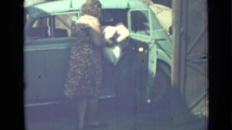The woman loads a pale bundle through the open rear door of the blue van in footage identified as 1967 Saint Petersburg.