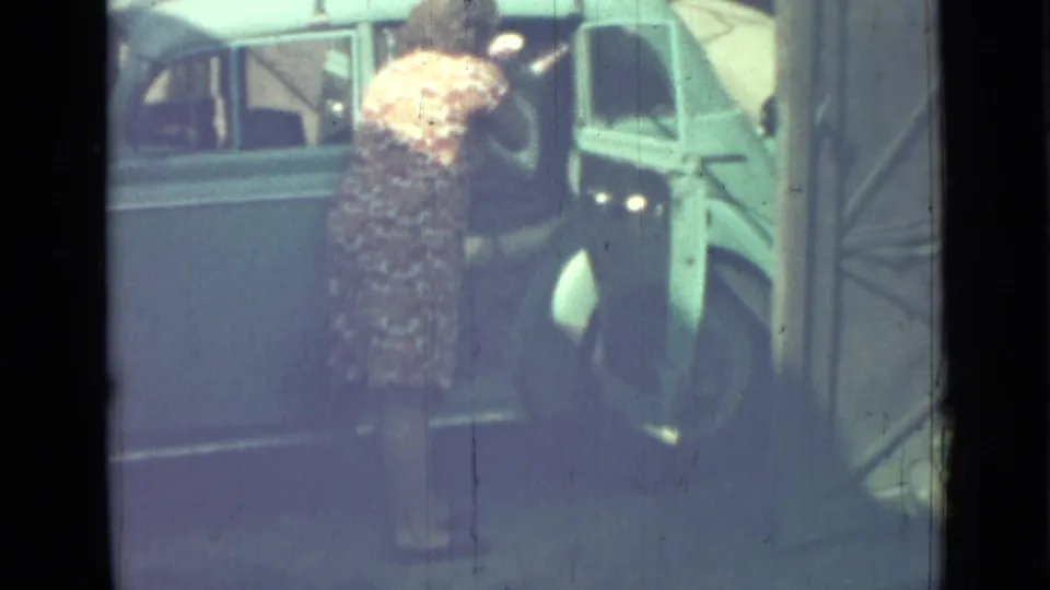 In this 1967 Saint Petersburg home-movie frame, a woman leans into the open door of a light blue sedan with a roof rack.
