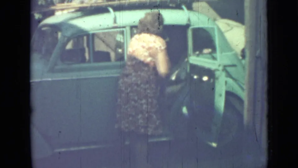 The woman remains beside the light blue sedan, with the open door and roof rack visible in the 1967 Saint Petersburg footage.