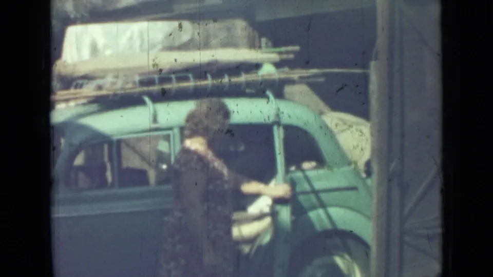 A 1967 Saint Petersburg frame shows the woman beside the blue sedan, appearing to handle or close a rear door.