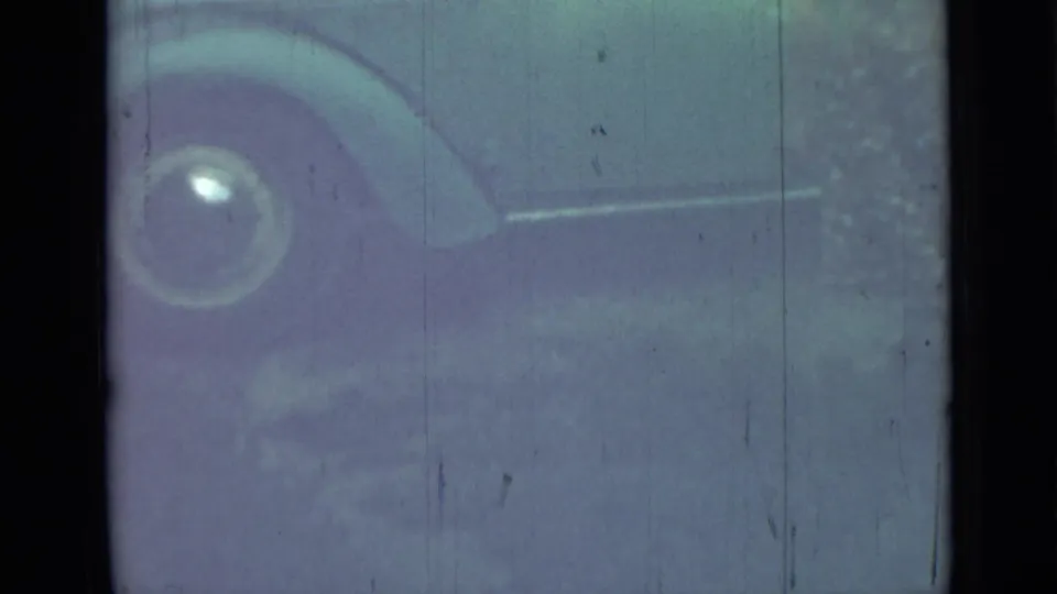 Grainy 1967 8mm frame from Saint Petersburg showing part of a parked vintage car with a rounded fender and hubcap.