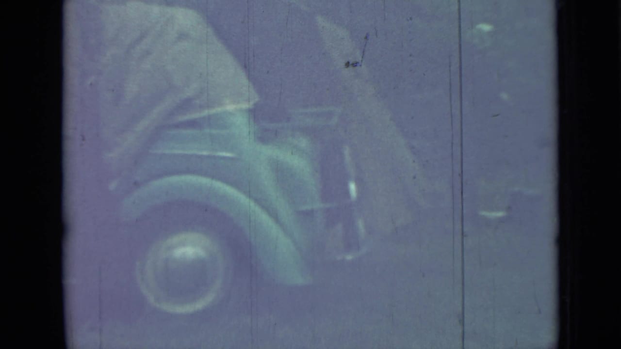 Person beside a vintage car with a rounded front fender and wheel visible.