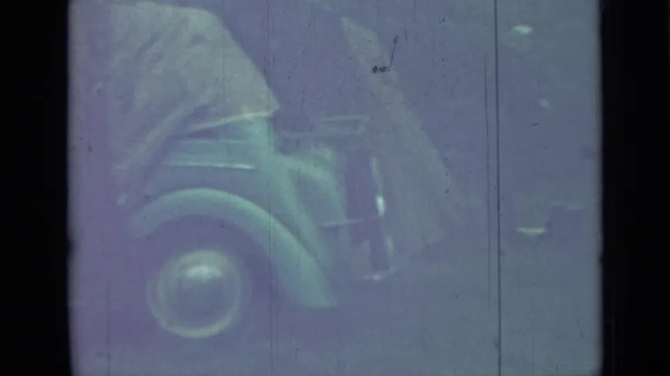 Grainy 1967 Saint Petersburg home-movie frame showing a person near a parked vintage car, partly obscured by fading and scratches.