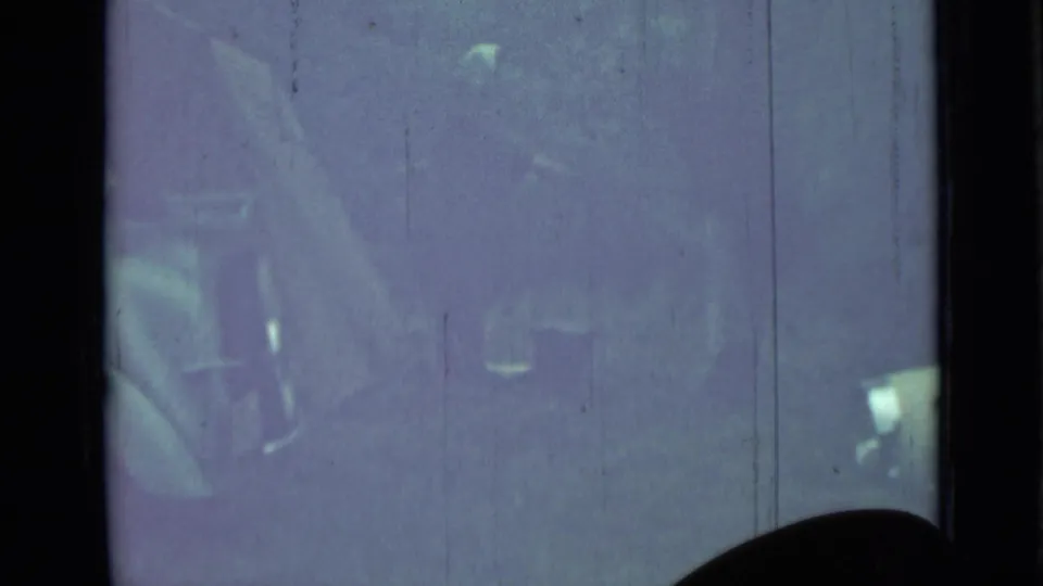 Faded 8mm frame from the 1967 Saint Petersburg clip, showing a person near a vintage car with indistinct belongings or vehicle details.