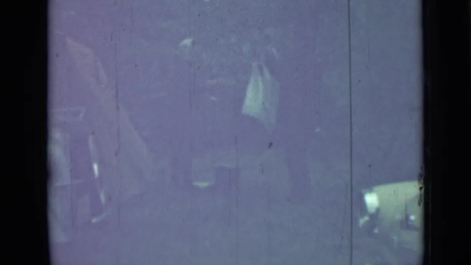 Very faded 1967 Saint Petersburg 8mm frame showing a person beside a car, with a small light object visible near the vehicle.