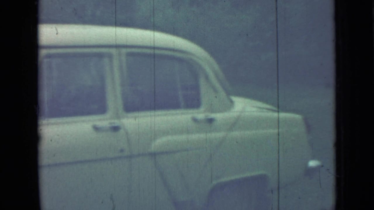 Pale vintage sedan seen from the side through soft 8mm film grain.