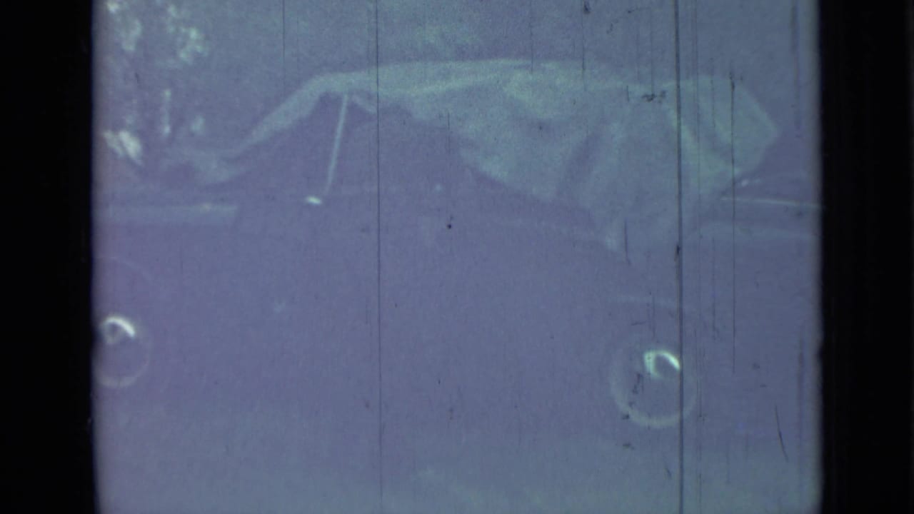 Dim close view of the car front area through scratched film and window glare.