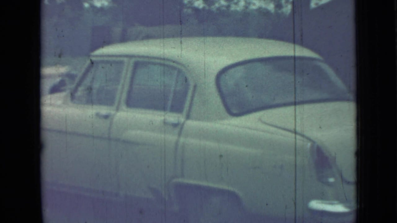 Pale vintage sedan seen from the rear side through a faded 8mm frame.