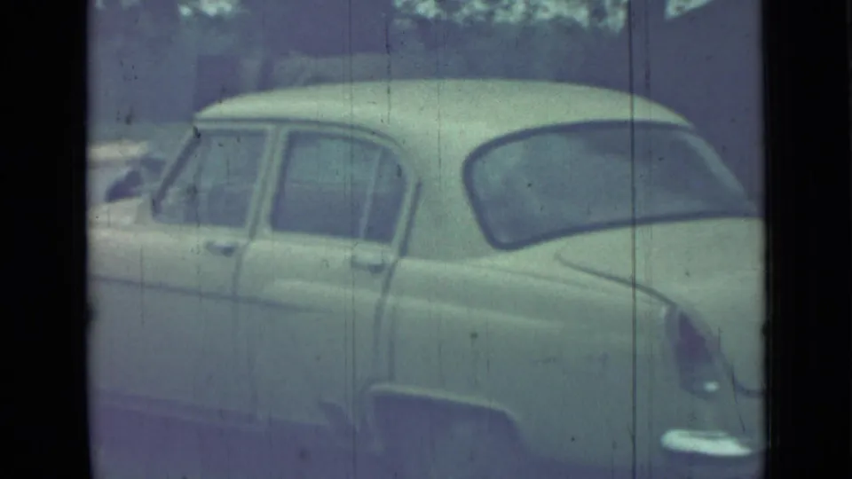 1967 Saint Petersburg home-movie frame showing a pale rounded sedan parked in a quiet lot, with soft focus and film scratches.