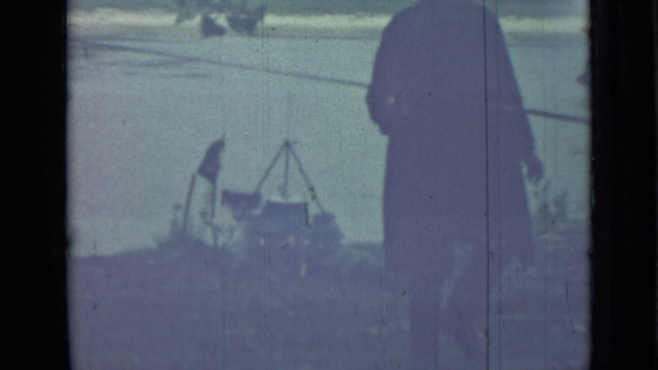 1967 Saint Petersburg 8mm frame with a dark-clothed man walking near grass, water, trees, and tripod-like equipment.