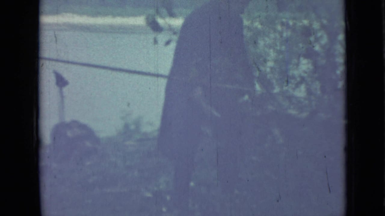 Dark figure holds an object while facing dense garden foliage.