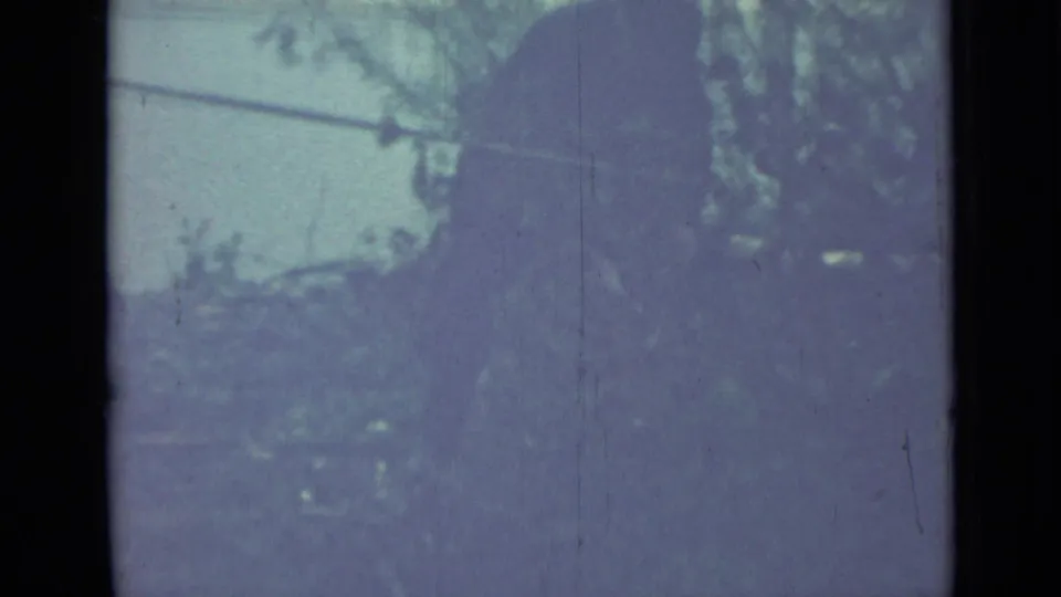 A soft, scratched 8mm frame shows the silhouetted person close to garden branches and overgrown vegetation.