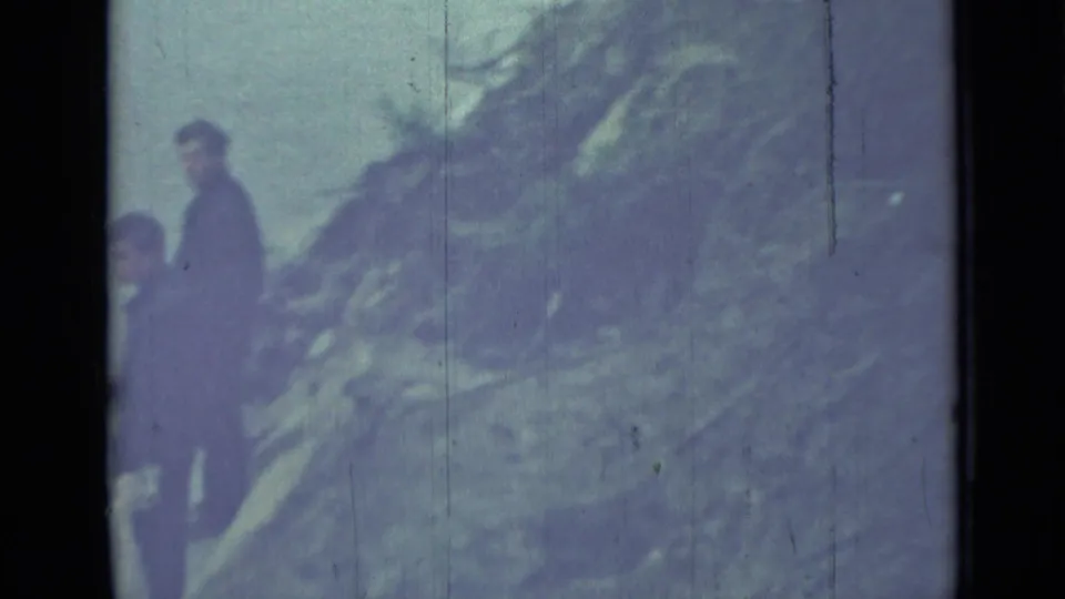 The men remain on the hillside in the Saint Petersburg home-movie scene, with foliage and sky softened by 8mm grain and exposure.