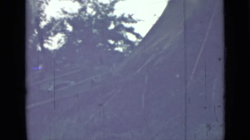 1967 Saint Petersburg-area home-movie frame showing a sloped, weathered vehicle-like surface amid dark forest vegetation.