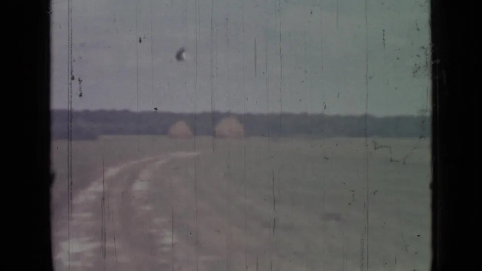 1967 8mm rural view near Saint Petersburg showing a winding dirt track, open field, distant mounds, and a small bird in flight.