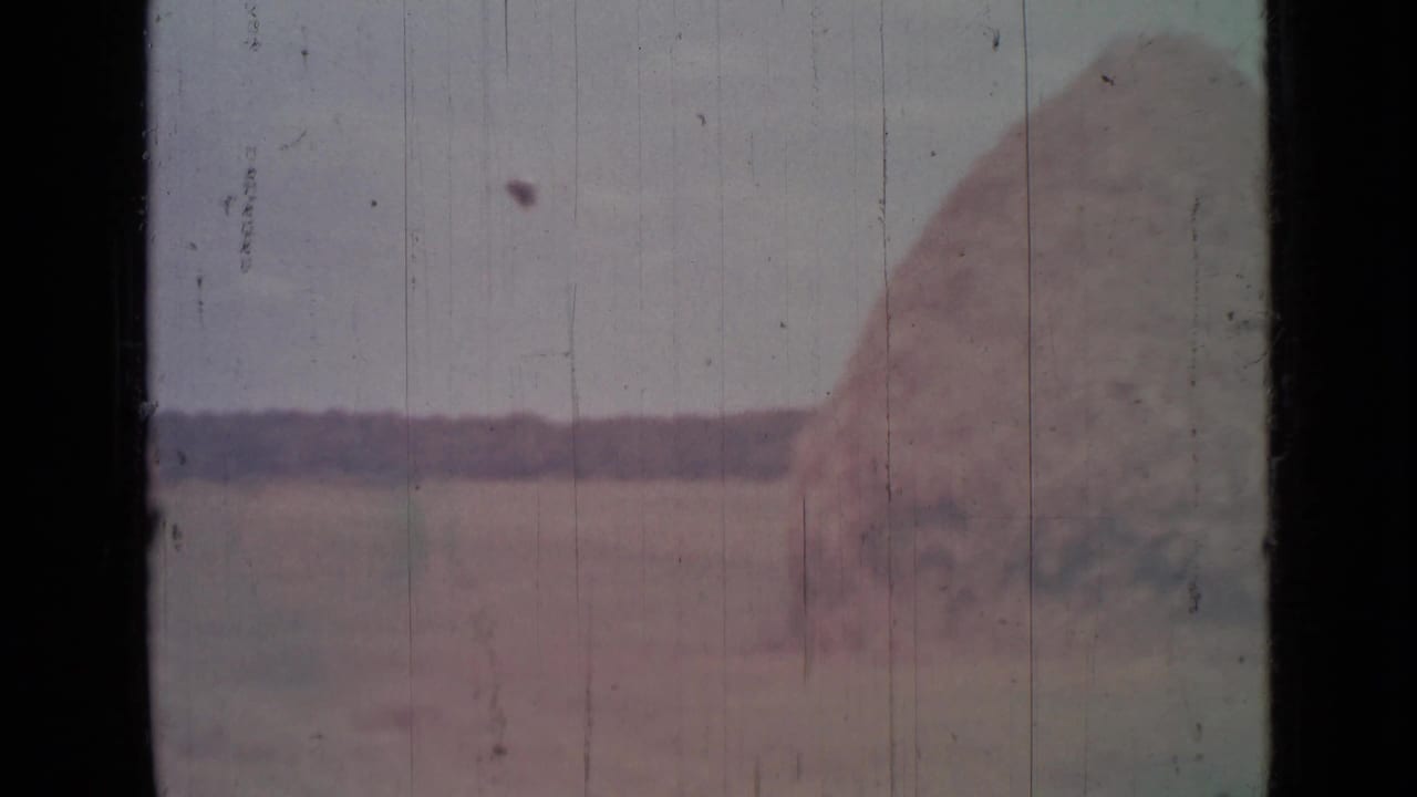 1967 8mm frame from near Saint Petersburg showing a large haystack or mound seen through a dark-edged vehicle window.