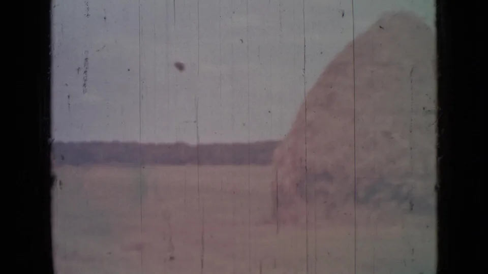 1967 8mm frame from near Saint Petersburg showing a large haystack or mound seen through a dark-edged vehicle window.