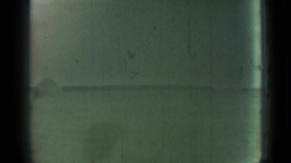 Green-tinted 8mm frame looking through glass across a flat rural field and low horizon.