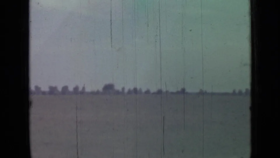 1967 8mm coastal view near Saint Petersburg, with flat water, a pale sky, and a faint tree-lined horizon softened by film wear.