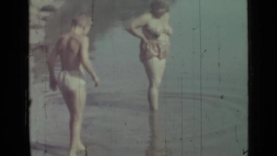 1967 Saint Petersburg home-movie frame with two beachgoers in shallow water, softly focused and partly faded.