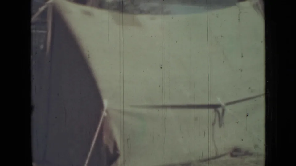 1967 8mm frame from Saint Petersburg metadata showing a close, soft-focus view of a green tent side with line and pole.