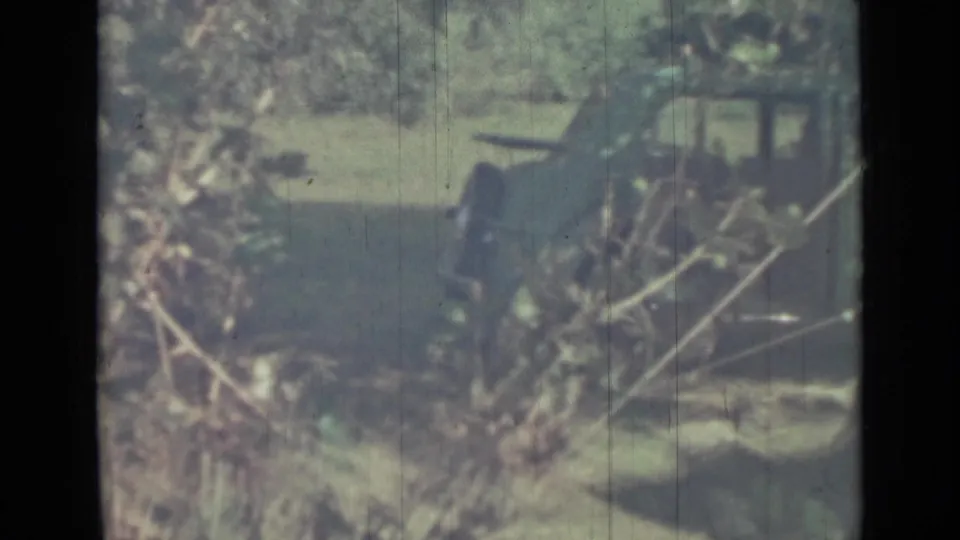 Wider 1967 8mm frame showing the green tent in a wooded outdoor area with grass, branches, and filtered light.