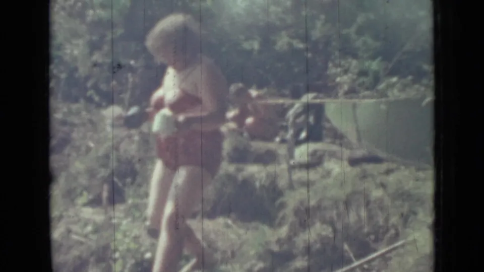 1967 Saint Petersburg frame showing a woman in a red bikini with a white container beside foliage and a horizontal branch or rail.