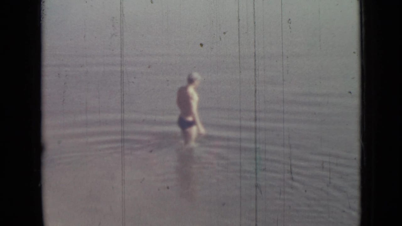 A boy in swim trunks stands in calm water in 1967 8mm home-movie footage identified as Saint Petersburg, Russia.