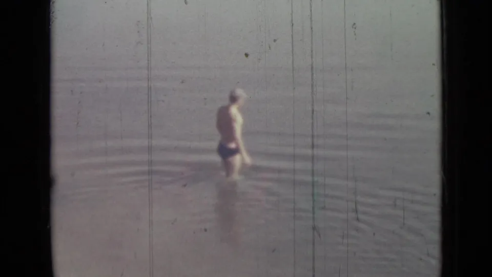 A boy in swim trunks stands in calm water in 1967 8mm home-movie footage identified as Saint Petersburg, Russia.