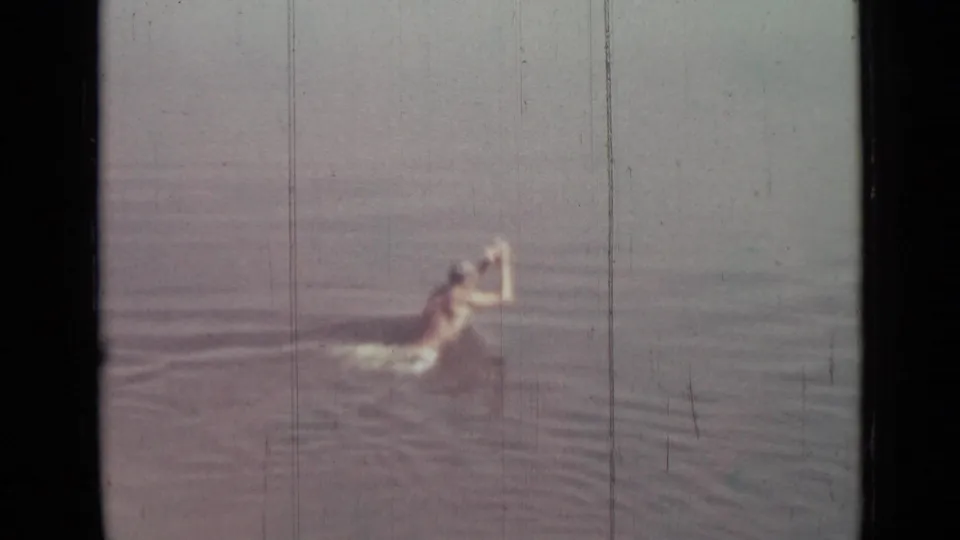 The boy moves through the water with one arm raised, creating a small splash in faded 8mm footage.