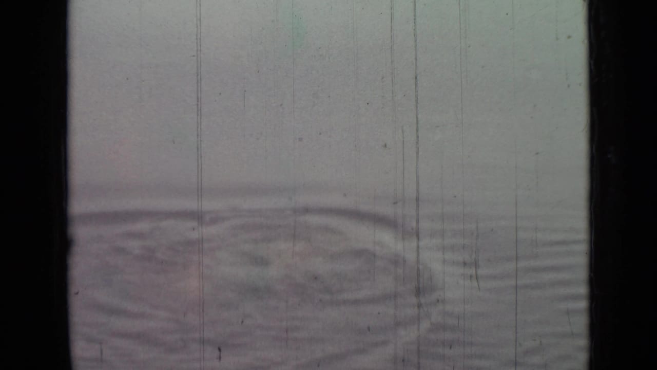 1967 8mm home-movie frame showing pale open water with a circular ripple pattern and visible film scratches.
