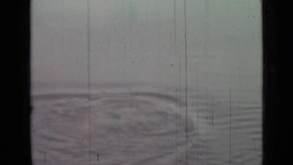 1967 8mm home-movie frame showing pale open water with a circular ripple pattern and visible film scratches.