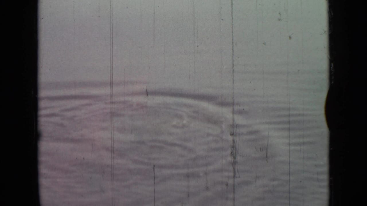 Water ripples spread across a foggy surface with film wear visible.