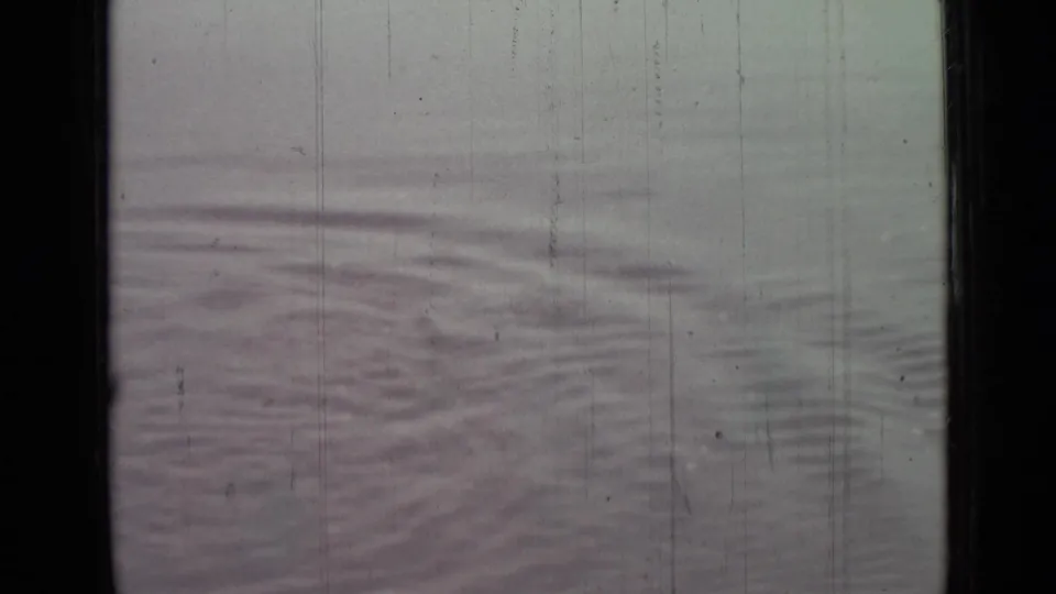 1967 8mm frame showing low water ripples on a fog-muted surface with scratches, dust, and faded color.