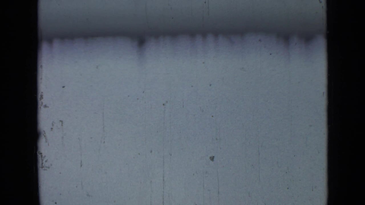A washed blue-gray sky fills the frame, with 8mm gate edges, scratches, and no clearly visible subject.
