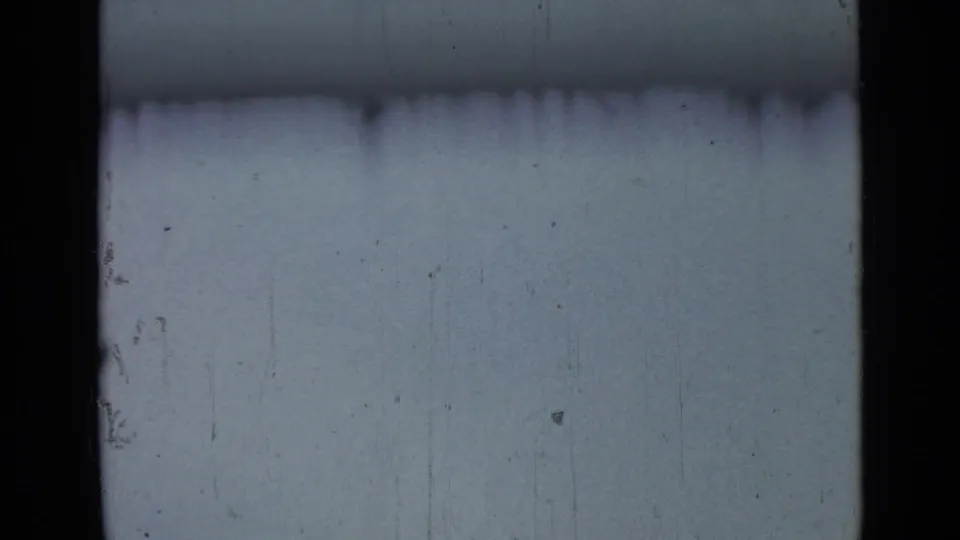 A washed blue-gray sky fills the frame, with 8mm gate edges, scratches, and no clearly visible subject.