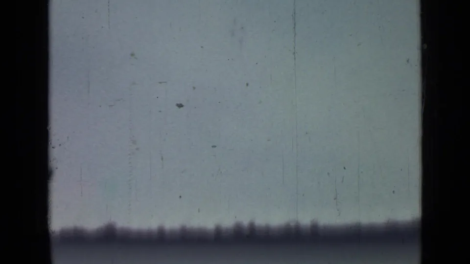 A pale outdoor sky fills the 8mm frame, with a blurred dark band near the bottom and visible scratches across the scan.