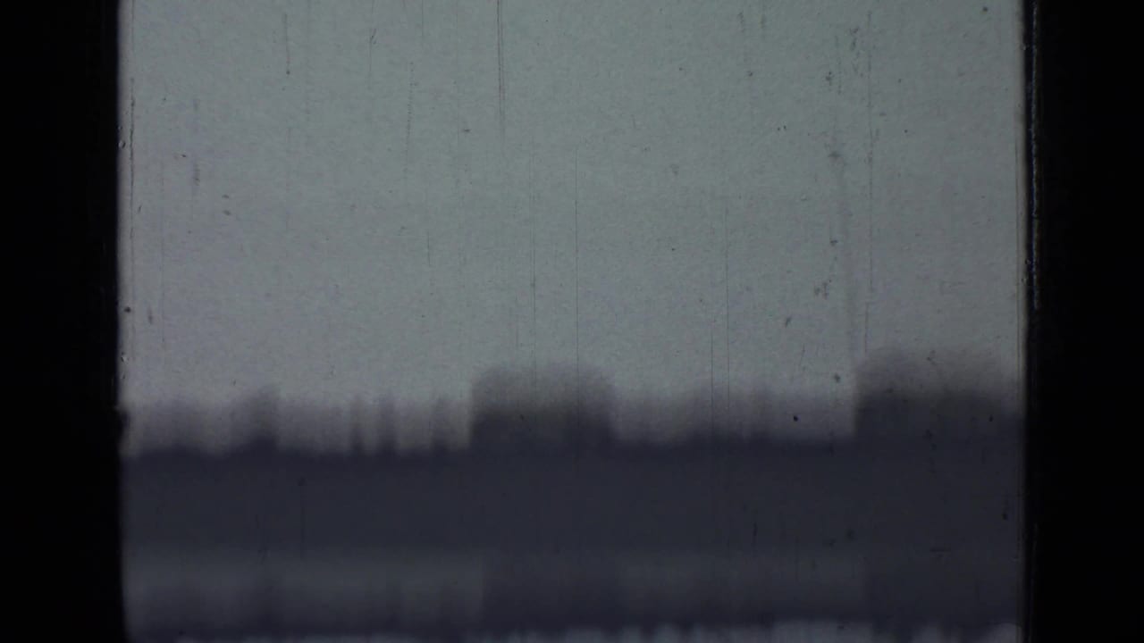 Dark film gate edges frame a hazy, scratched view with an indistinct horizon.