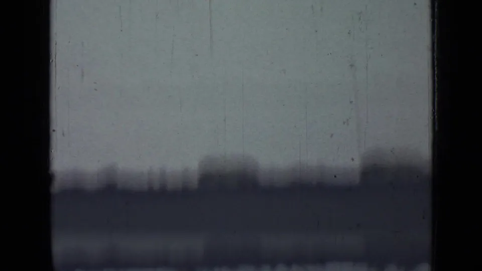 1967 8mm frame from Saint Petersburg showing haze, scratches, gate edges, and a barely visible distant outdoor scene.