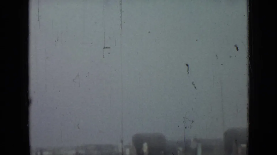 Hazy 1967 Saint Petersburg home-movie frame with a grassy field, distant arched structure, scratches, and soft exposure.