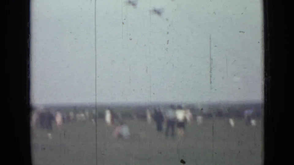 A 1967 Saint Petersburg airshow view shows scattered spectators in a grassy field beneath aircraft flying in formation.