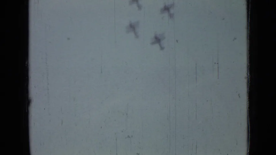 The frame emphasizes aircraft in formation against the sky, with only the lower field area faintly visible through the 8mm scan.