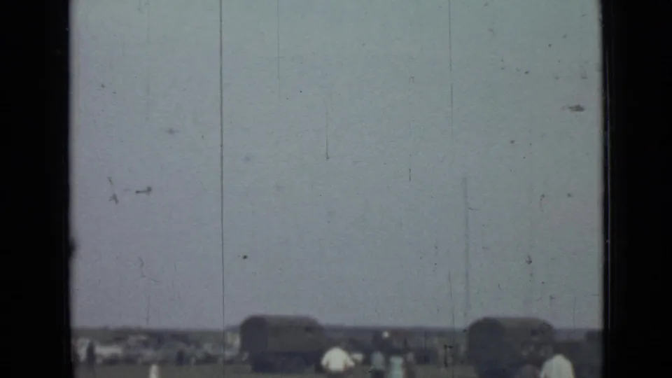 Soft 8mm view of distant military trucks and visitors along an open field in Saint Petersburg, Russia, in 1967.